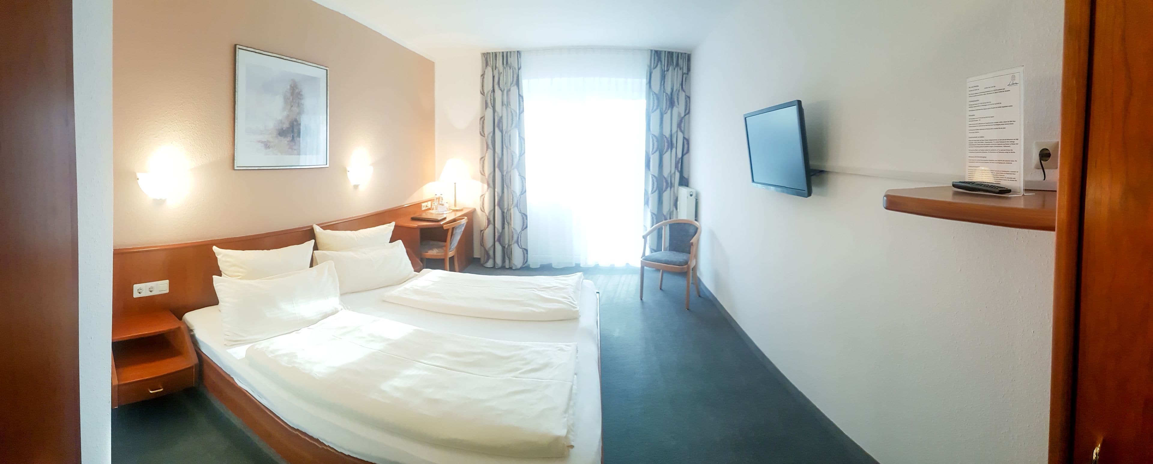 Una habitación de hotel con una cama grande, mesitas de noche, televisor y ventana con cortinas.