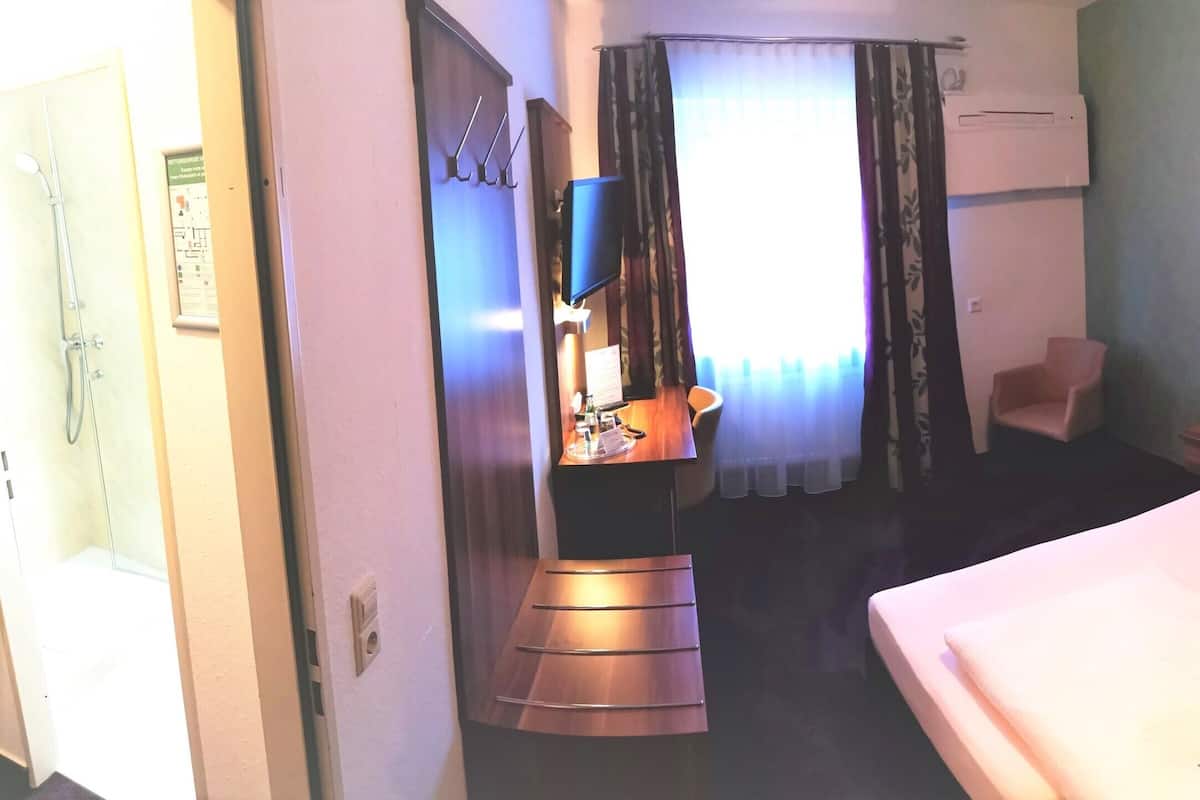A hotel room with a large bed, a chair, a desk with a flat-screen TV, and a shower area.