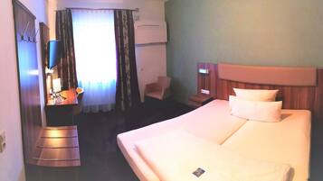 A hotel room with a large bed, a chair, a desk with a flat-screen TV, and a shower area.