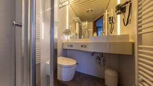 A modern bathroom with a glass shower enclosure, a white toilet, a vanity with a mirror, and a towel rack. - Hotel Löwen (Meckenbeuren)