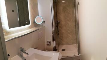 A modern bathroom with a white sink, a mirror with a round light, and a glass-enclosed shower.
