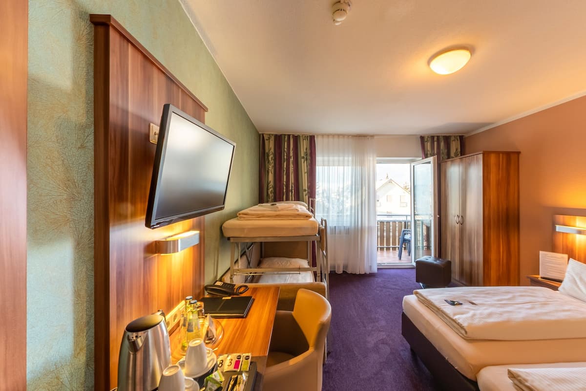 A hotel room with a bed, a desk with a flat-screen TV, a chair, a small table with toiletries, and a balcony with a view.