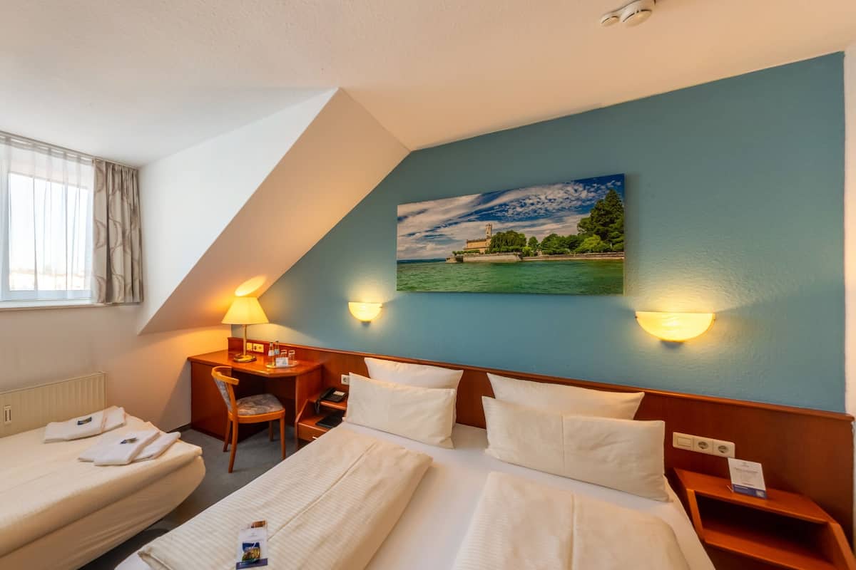 A hotel room with two beds, a desk, a chair, and a painting on the wall.