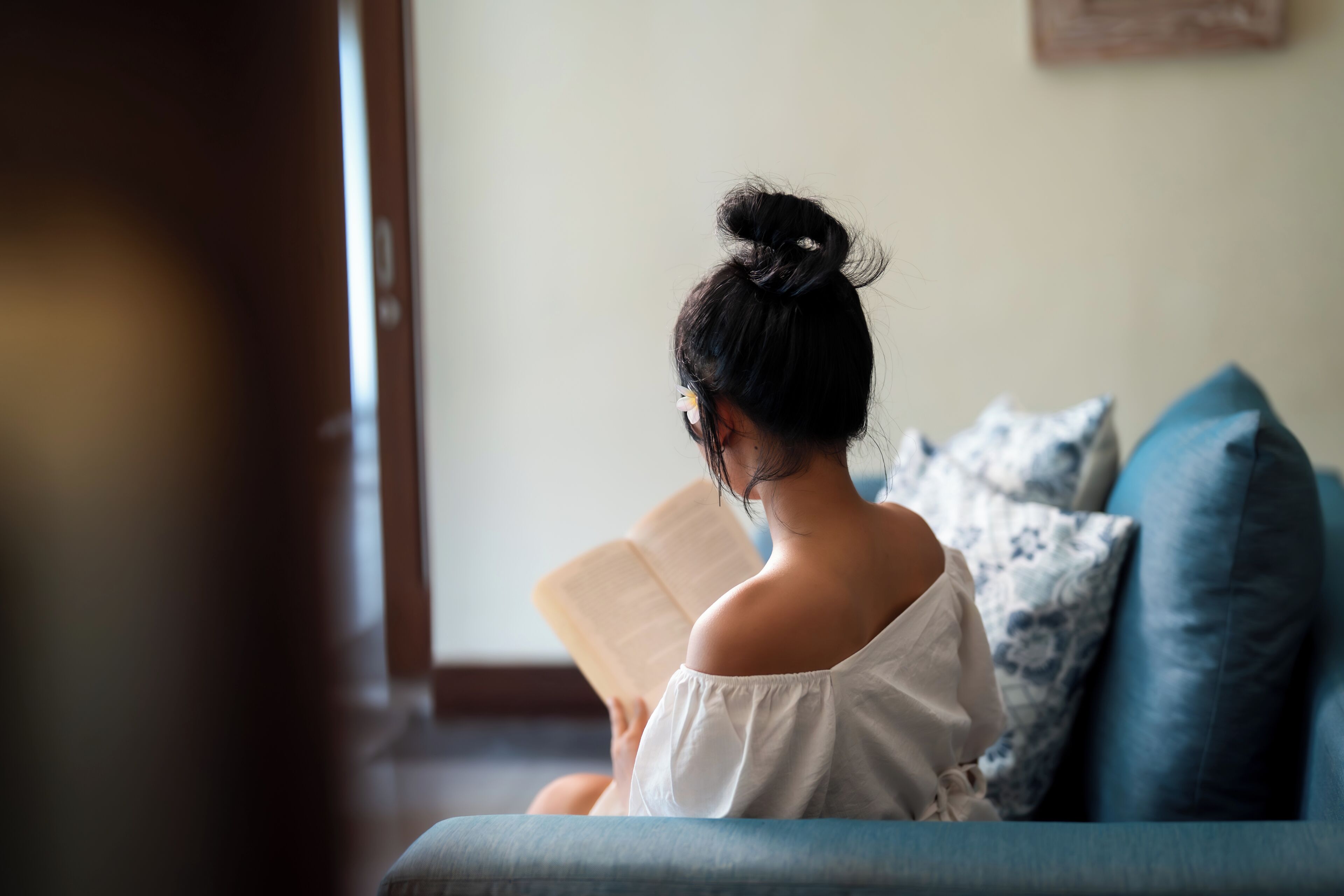 Eine Person sitzt auf einem blauen Sofa und liest ein Buch.