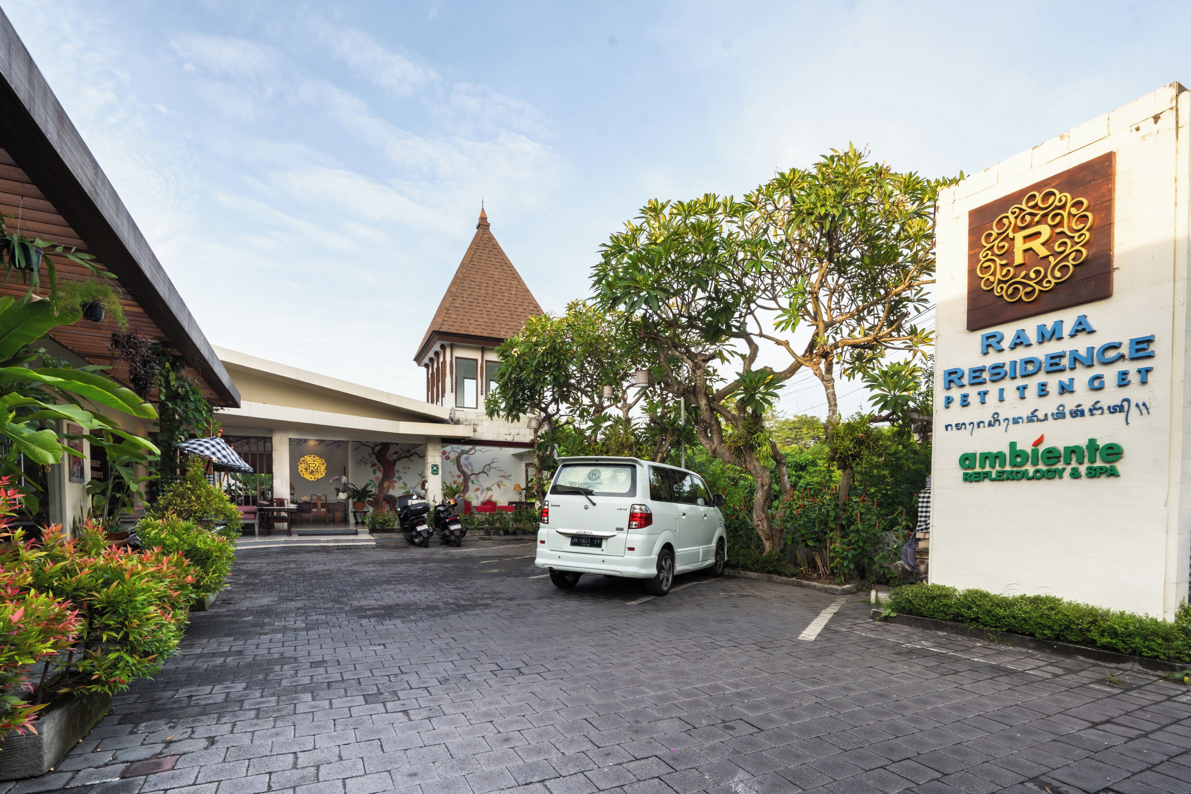 A parking area with a white car, a building with a pointed roof, and a sign for Rama Residence with a logo and text.