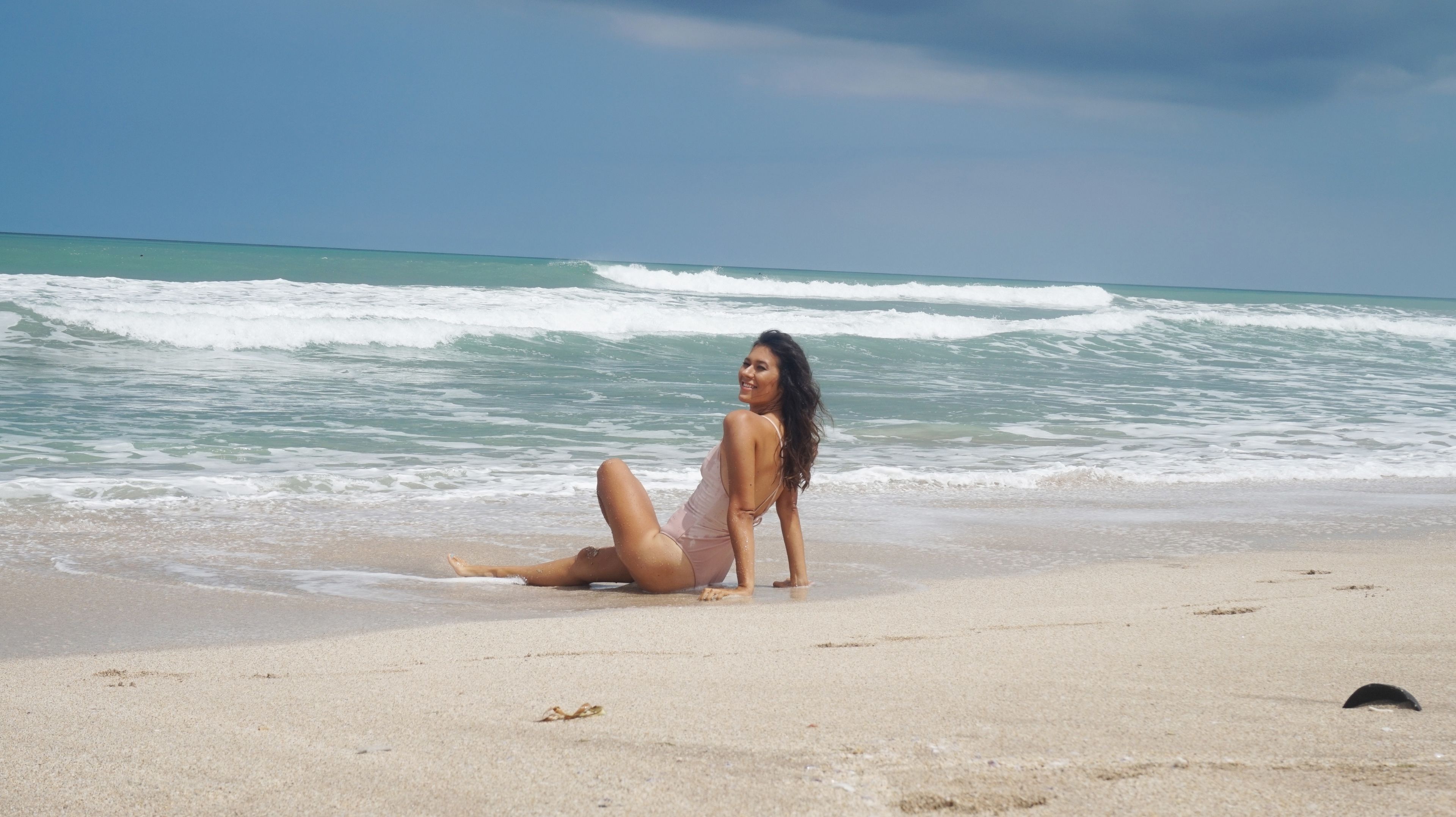A beach with waves and a person sitting on the sand.