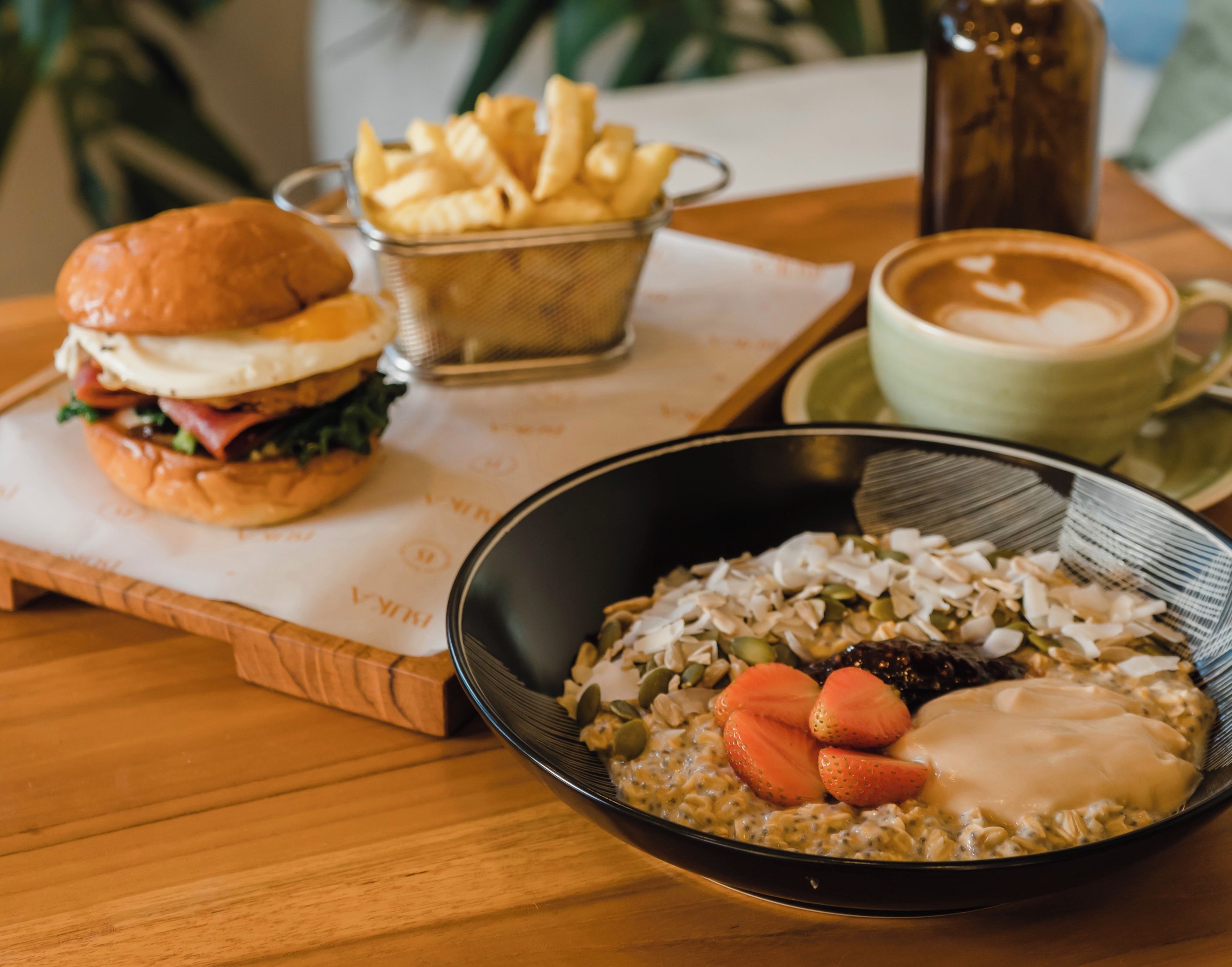 Una comida que incluye una hamburguesa, papas fritas, una taza de café y un tazón de avena con frutas y nueces.
