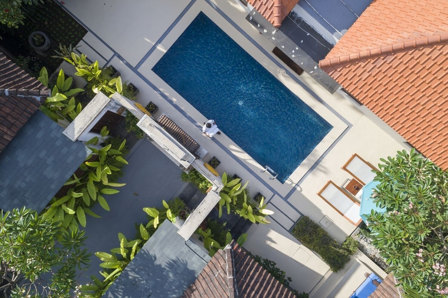 Luftaufnahme eines Wohngebiets mit einem Schwimmbad, Blumentöpfen und einer Person, die gerade geht.