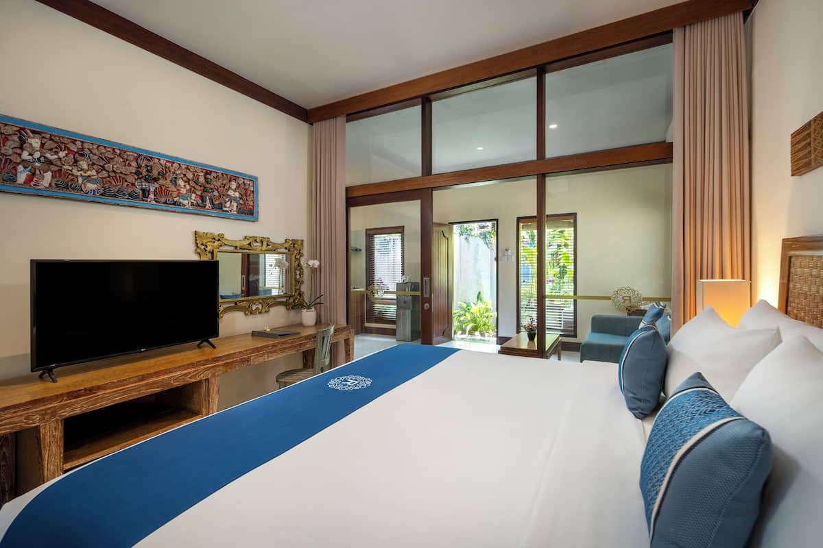 A hotel room with a large bed, a television, a desk, and a view of the outdoors through large windows.