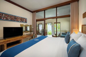 A hotel room with a large bed, a television, a desk, and a view of the outdoors through large windows.