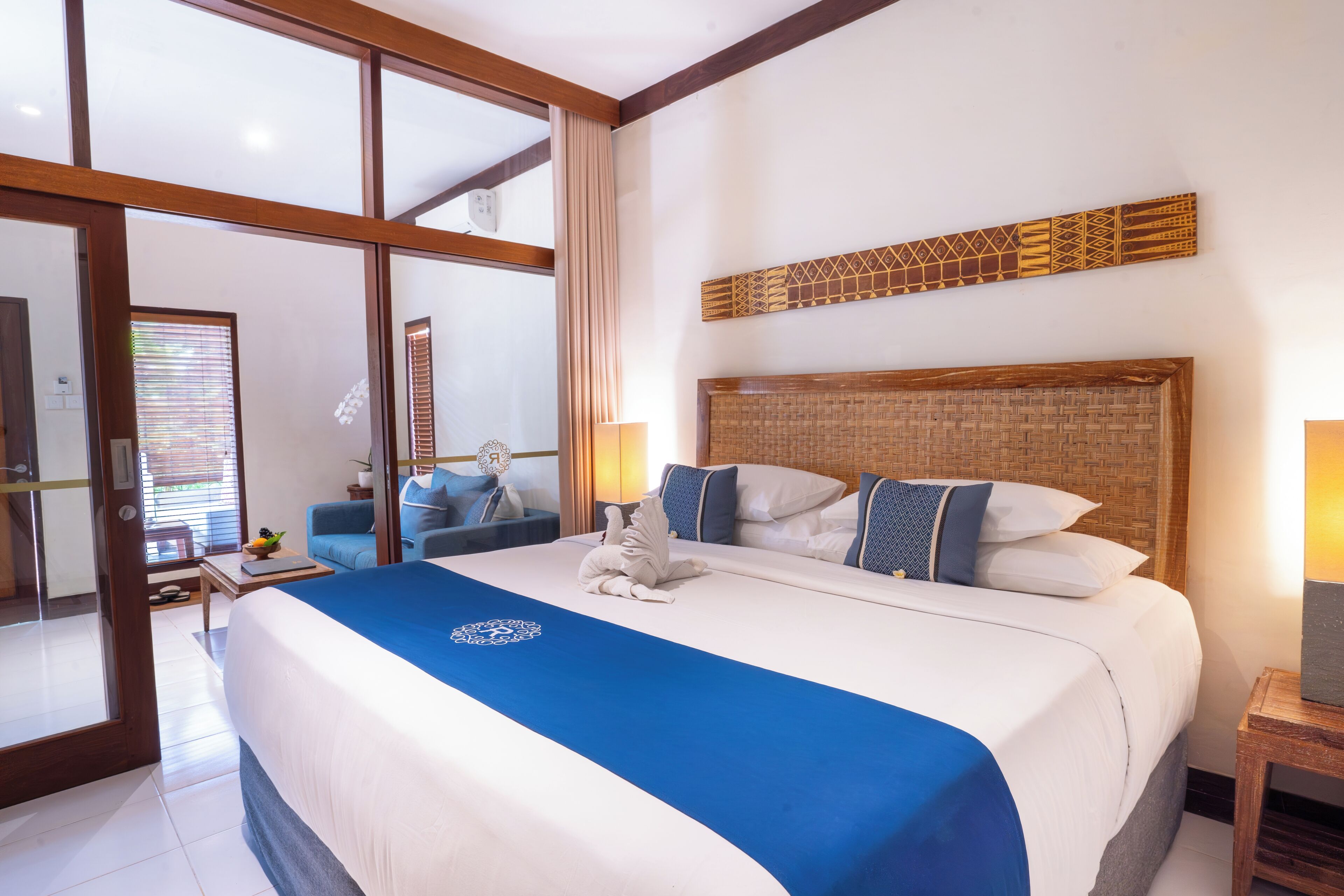 Ein Hotelzimmer mit einem großen Bett, einem hölzernen Kopfteil, einer blauen Bettdecke und einer Wanddekoration.