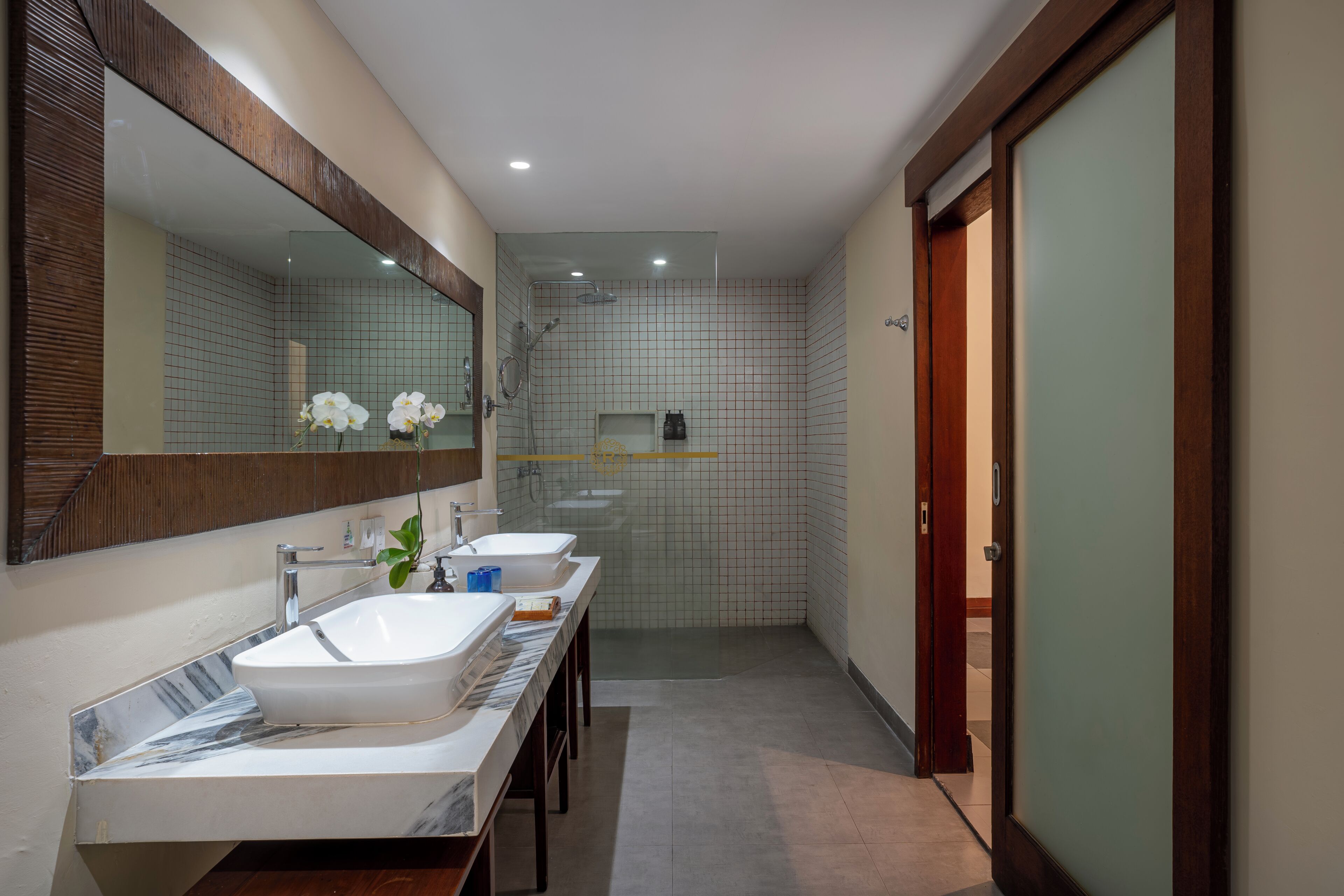 A modern bathroom with two sinks, a shower, and a large mirror.