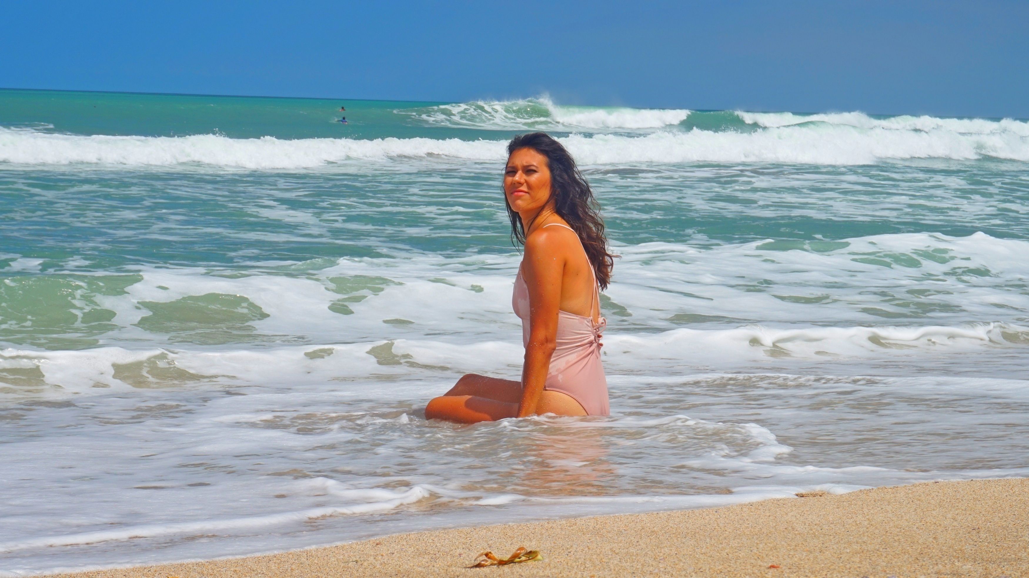 Une personne assise sur une plage de sable, avec des vagues en arrière-plan.