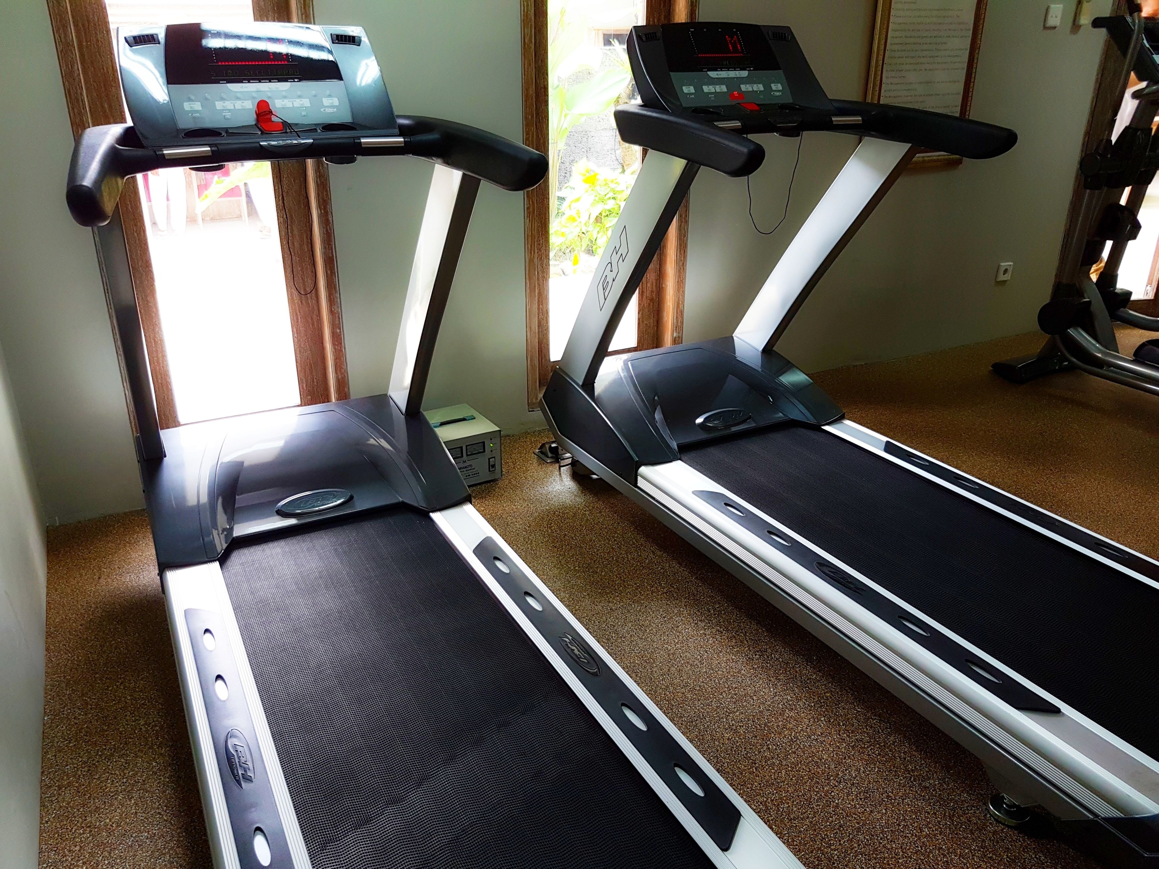 Two treadmills in a room with a carpeted floor and a window.