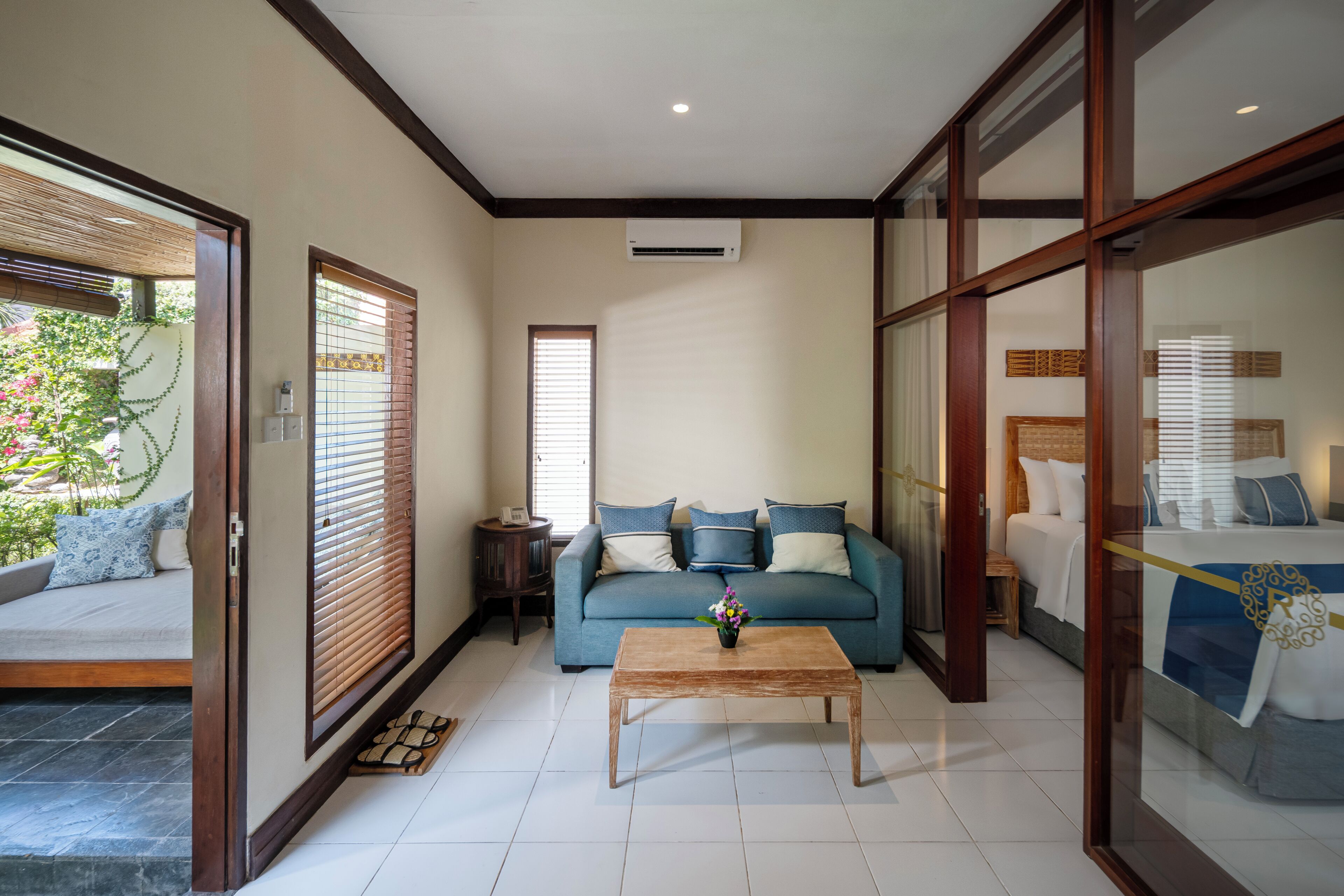 A room with a sofa, a coffee table, and a bed with a blue bedspread.