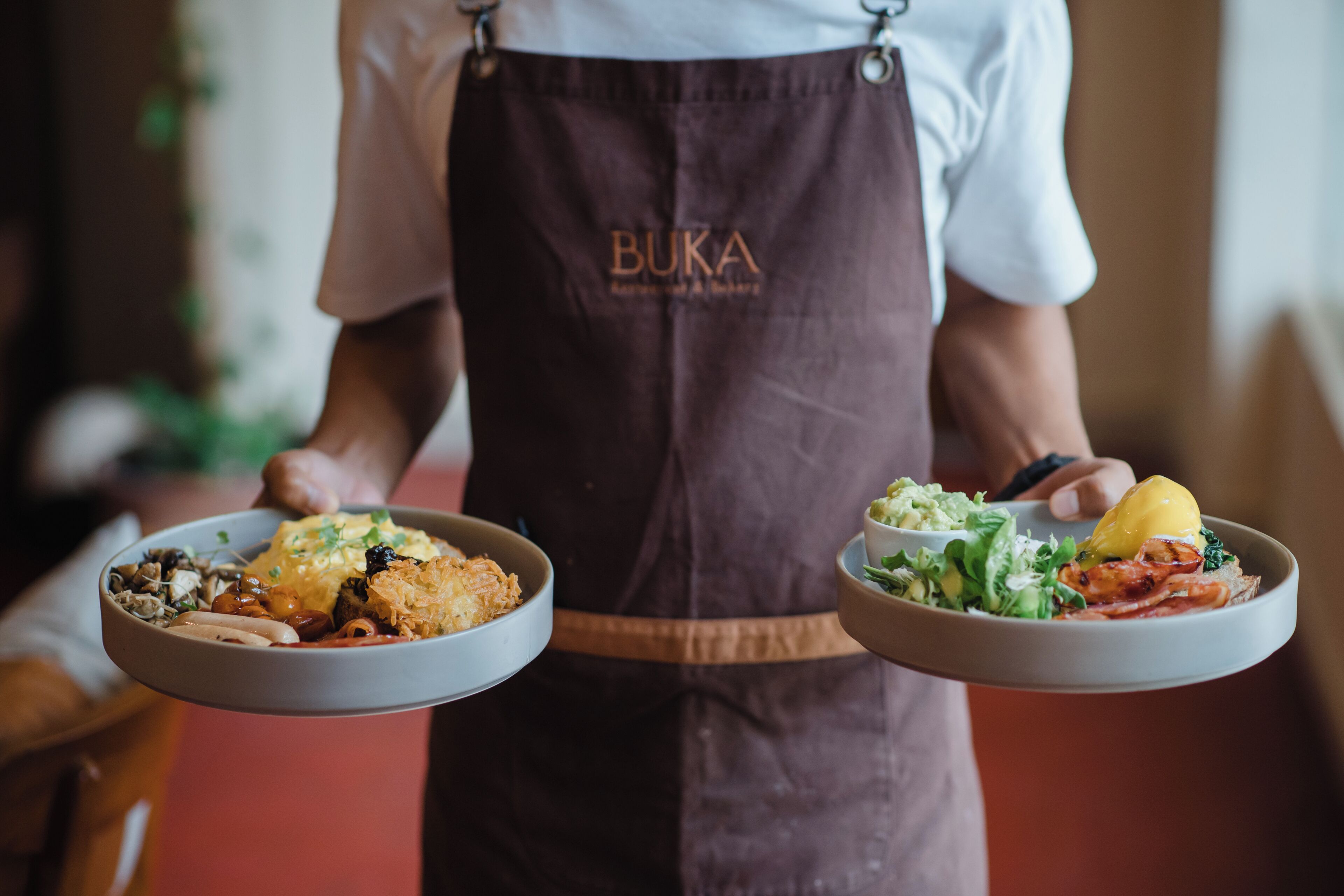 A person holding two plates of food, one with a salad and the other with a variety of dishes.