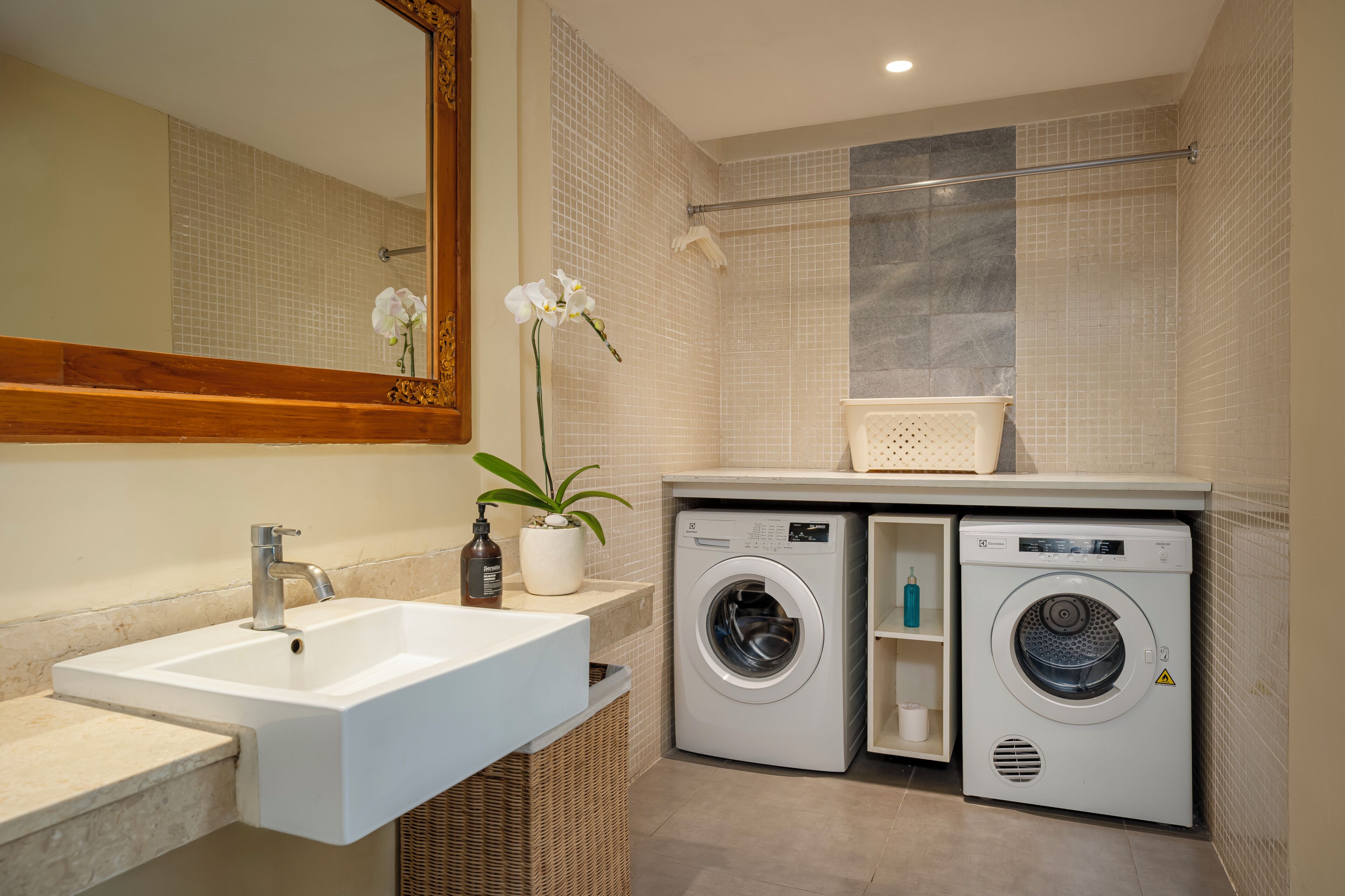 A bathroom with a sink, two washing machines, a mirror, and a potted orchid.