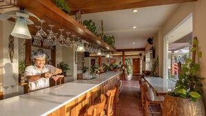 A bar area with wooden chairs, a long counter, and hanging wine glasses.