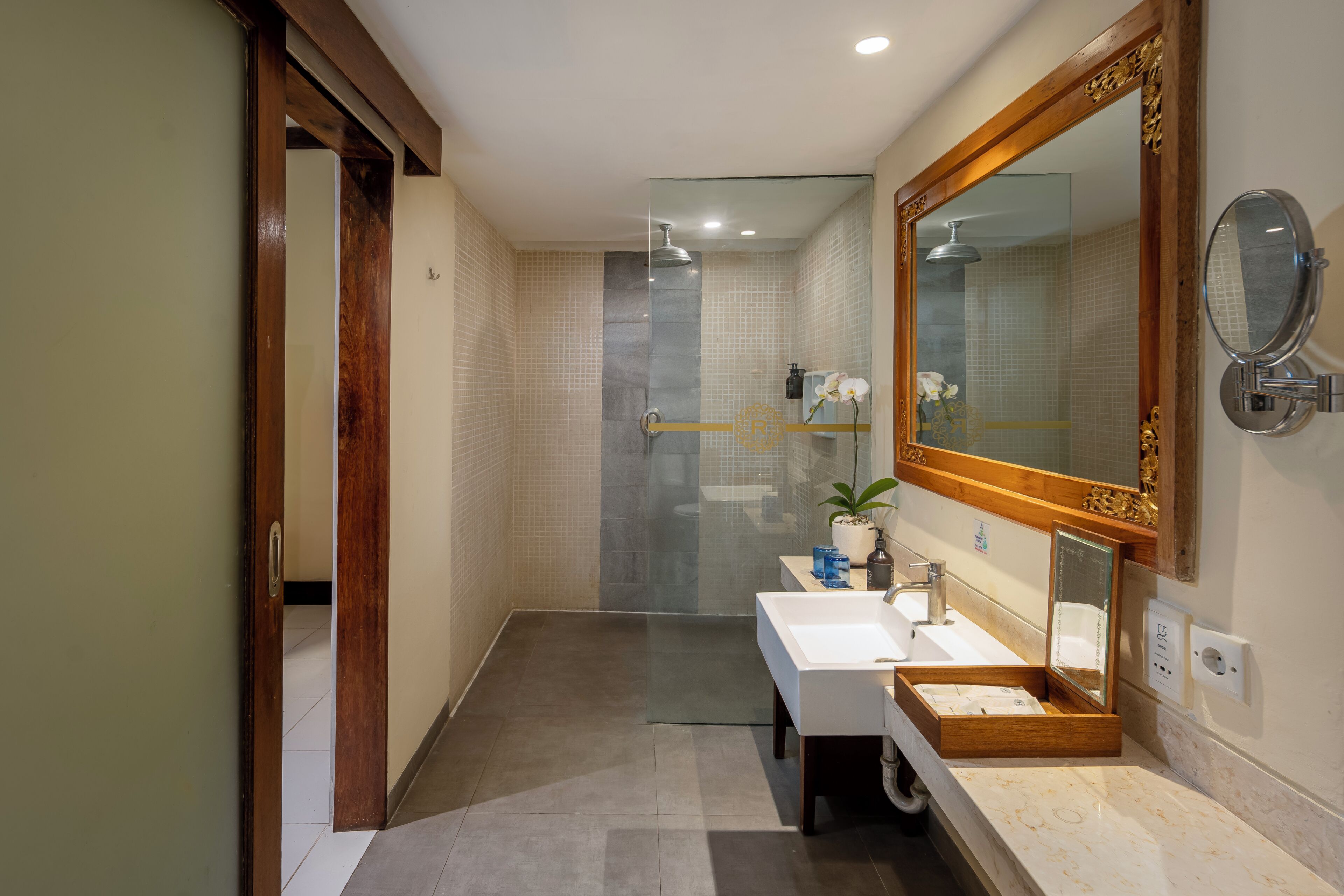 Une salle de bain moderne avec une douche à l’italienne en verre, un grand miroir et un lavabo blanc.