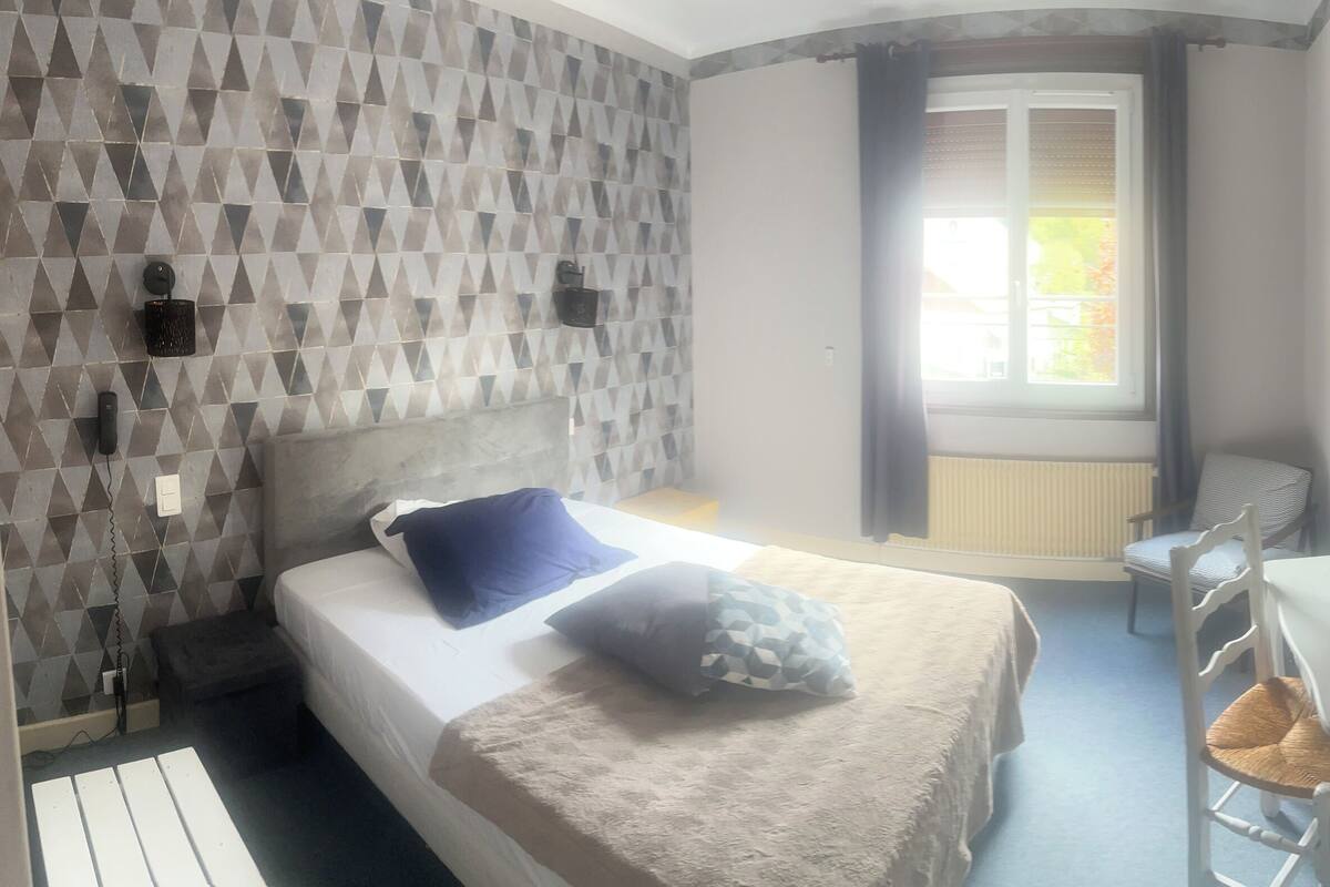 A bedroom with a bed, a desk with a chair, a window with curtains, and a wall-mounted TV.