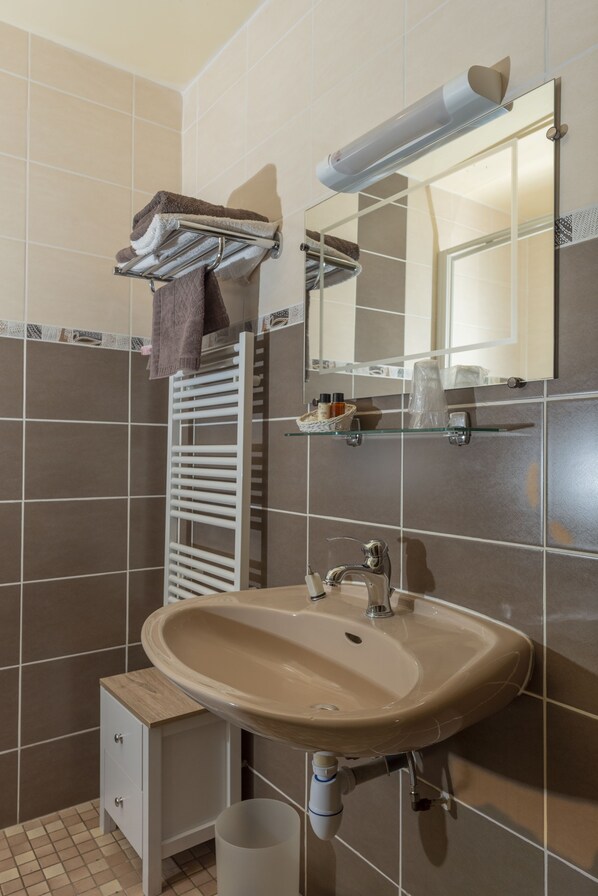 A bathroom with a beige sink, a mirror, a towel rack, and a small cabinet.