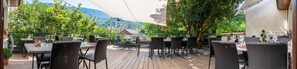 An outdoor patio with tables and chairs, surrounded by greenery and a mountain view. - Hôtel du Sorgia (Valserhône)