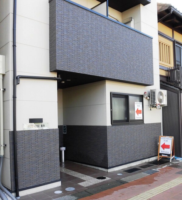 Un edificio con fachada de ladrillo, una ventana pequeña y un cartel que indica la entrada a Kyoto House Toji.
