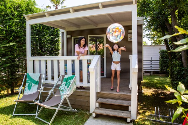 A covered porch with a white railing, a wooden deck, and a green chair with a white cushion. - Don Antonio Glamping Village (Giulianova)