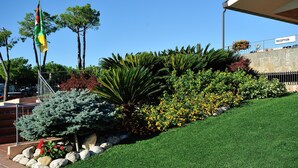 A landscaped area with a reception sign, a flagpole, and various plants including a large conifer and yellow flowering bushes.