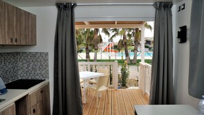 A balcony with a view of a pool and palm trees, a white table and chair, and wooden cabinets.