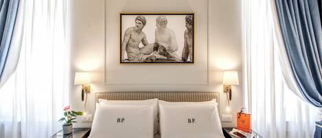 Habitación de hotel con cama, dos mesitas de noche, un cuadro enmarcado sobre la cama y una ventana con cortinas.