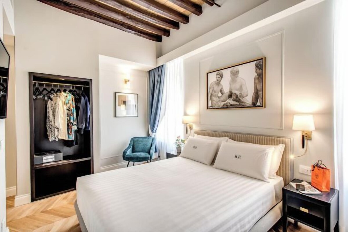 Una camera d'albergo con un letto, un armadio, una sedia, un quadro e un comodino.