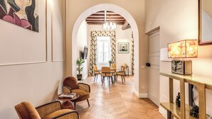 Amplia sala de estar con suelo de espiga, una mesa de comedor con sillas, un sofá y una consola con objetos decorativos.