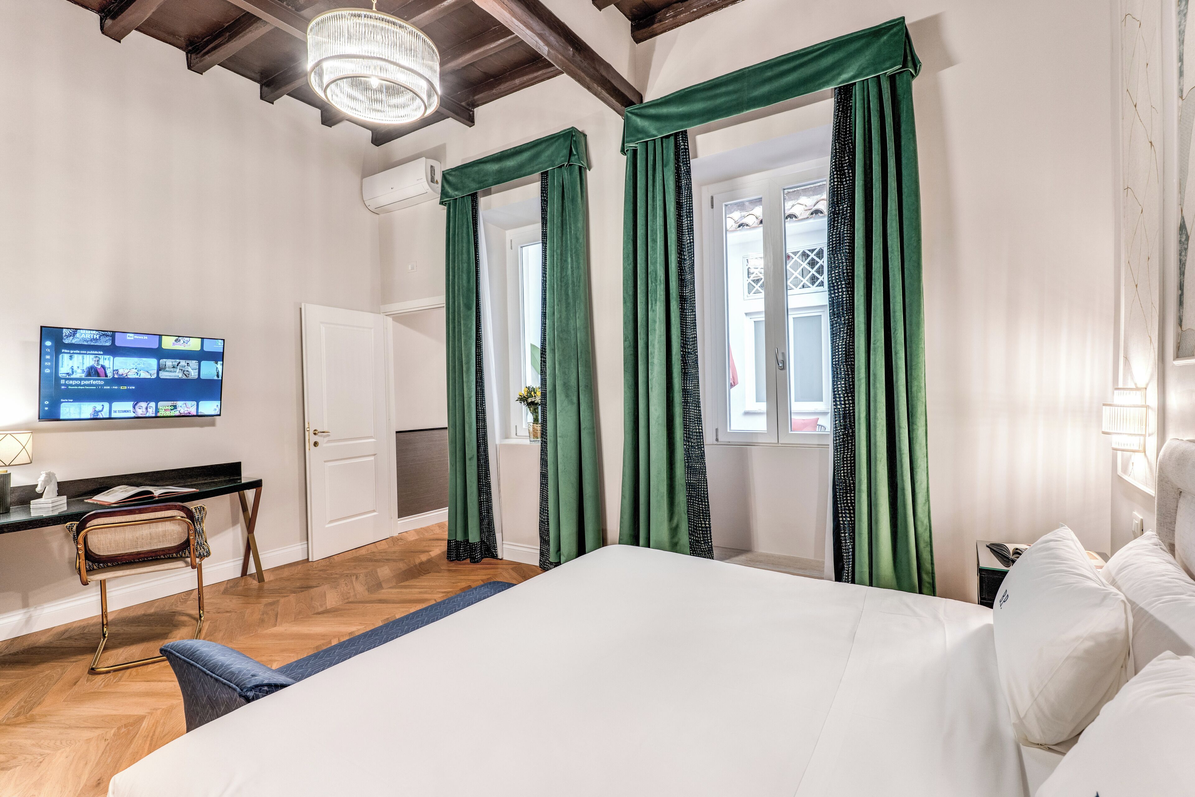 Ein Hotelzimmer mit Bett, Schreibtisch mit Computer, Stuhl und grünen Vorhängen.