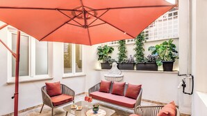 Un patio con muebles de mimbre, una mesa de vidrio y un paraguas rojo grande.