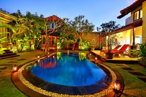 Una piscina rodeada por un jardín con plantas y un pabellón.