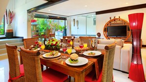 A dining area with wicker chairs, a wooden table set with plates of food, glasses of beverages, and a red curtain.