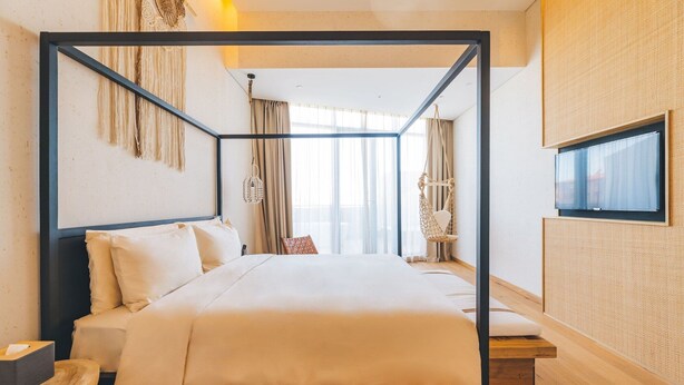 Una habitación de hotel moderna con cama con dosel, un ventanal con cortinas, un sillón colgante y un televisor montado en la pared.