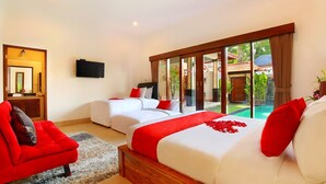 A hotel room with two beds, a TV, a red sofa, and a view of a swimming pool. - Villa De Liza Seminyak Beachside (Seminyak)