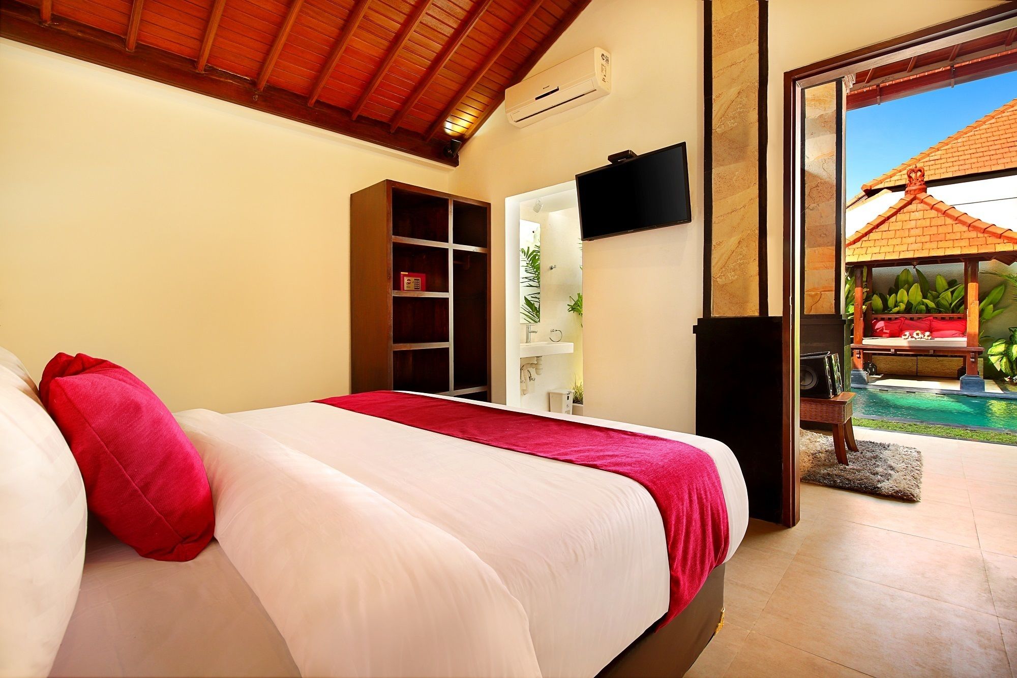 A bedroom with a bed, a TV, a bookshelf, and a view of an outdoor pool area.