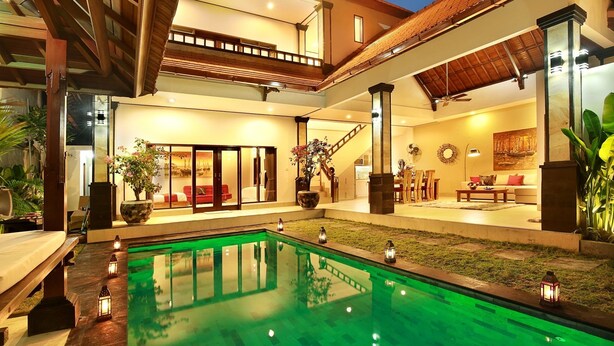 A spacious indoor pool area with a clear view of the adjacent living room, featuring a sofa and dining table. - Villa De Liza Seminyak Beachside (Seminyak)