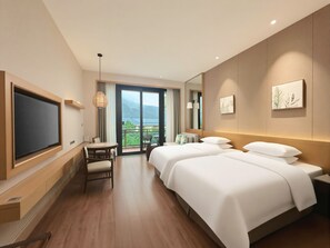 A hotel room with a large TV, a balcony with a view, two beds, a desk, and a chair.