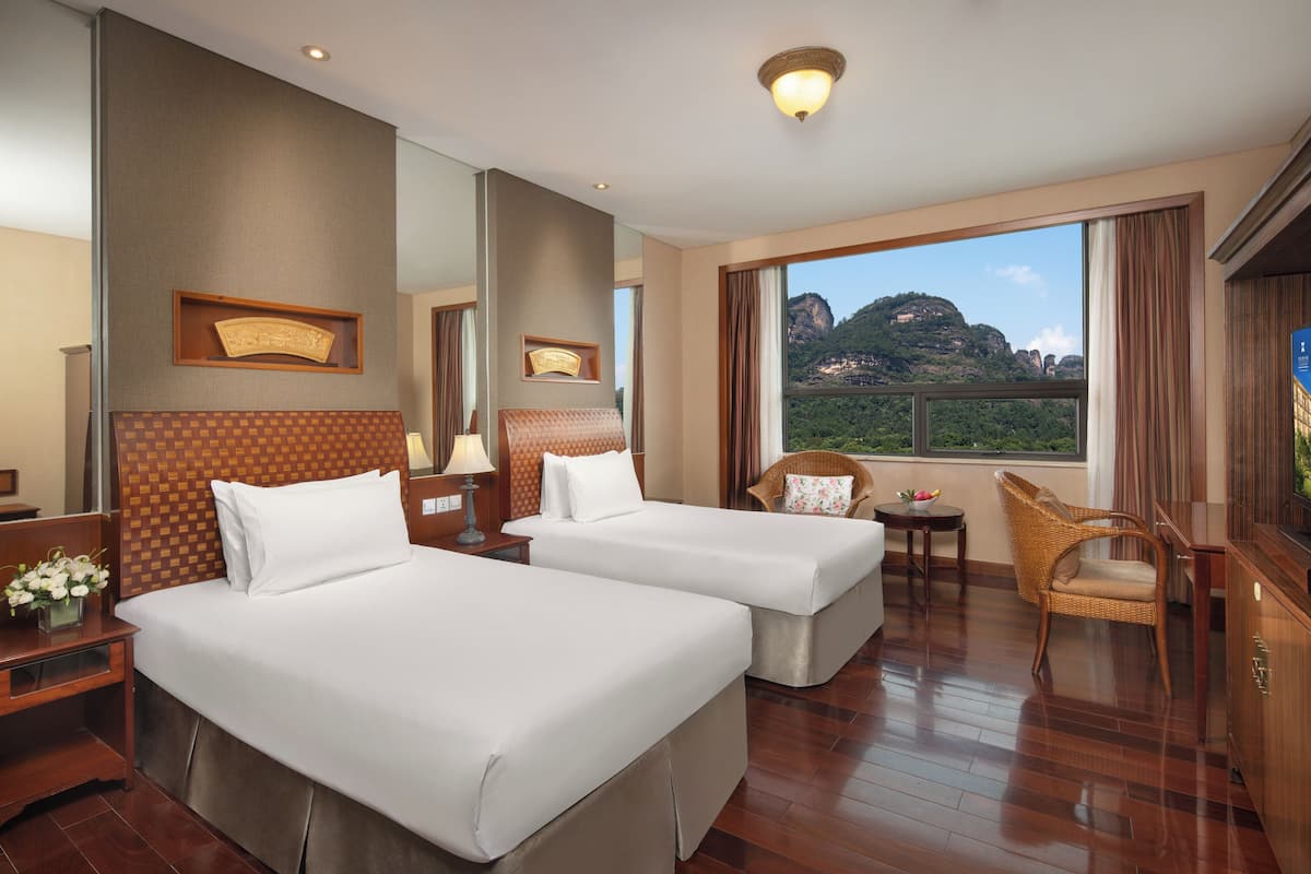 A hotel room with two beds, a large mirror, a view of a mountain, and a wooden floor.
