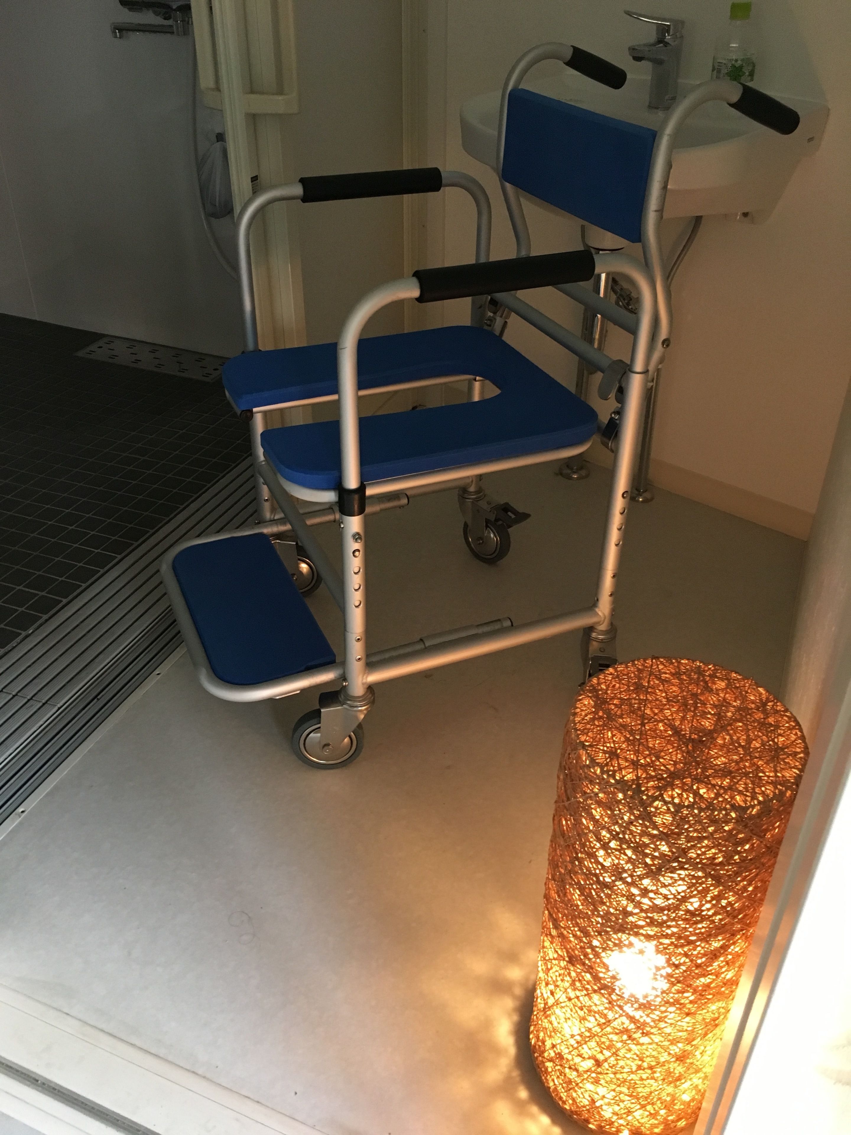 A wheelchair with blue seats and a metal frame, positioned next to a white sink and a door.