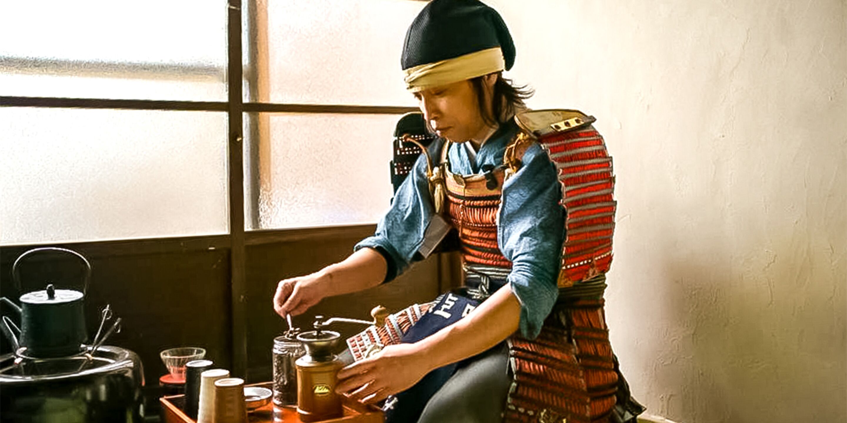 Une personne vêtue d’un costume traditionnel, en train d’utiliser un moulin à café et une bouilloire.