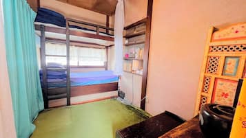 Un dormitorio con literas, un escritorio pequeño, una silla y un estante con libros y objetos personales.