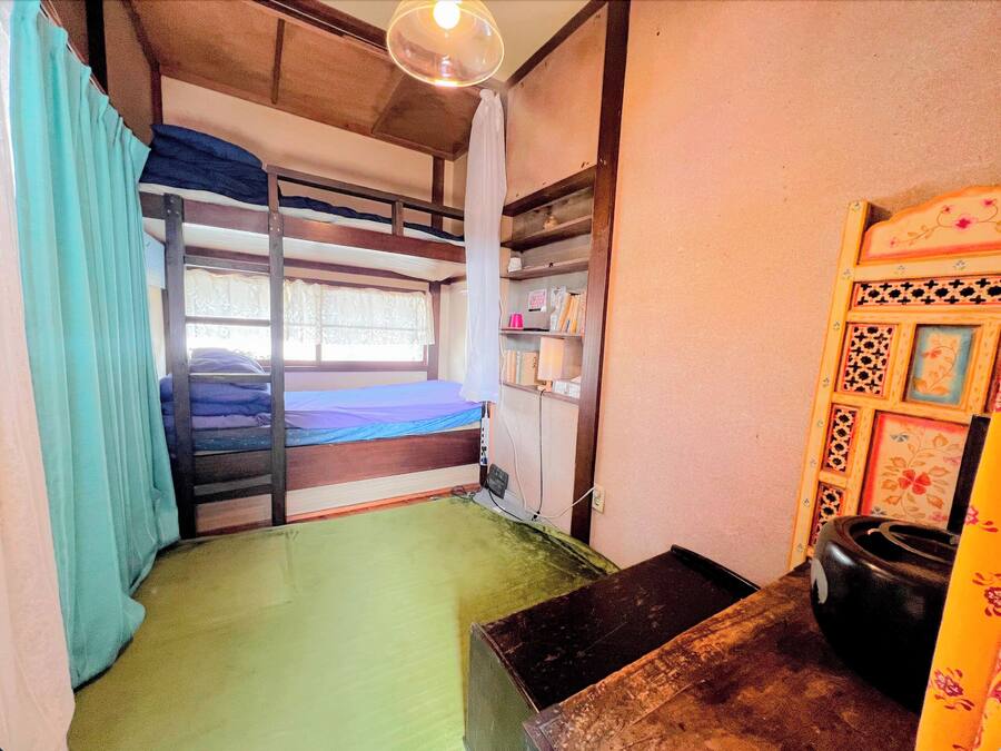 Un dormitorio con literas, un escritorio pequeño, una silla y un estante con libros y objetos personales.