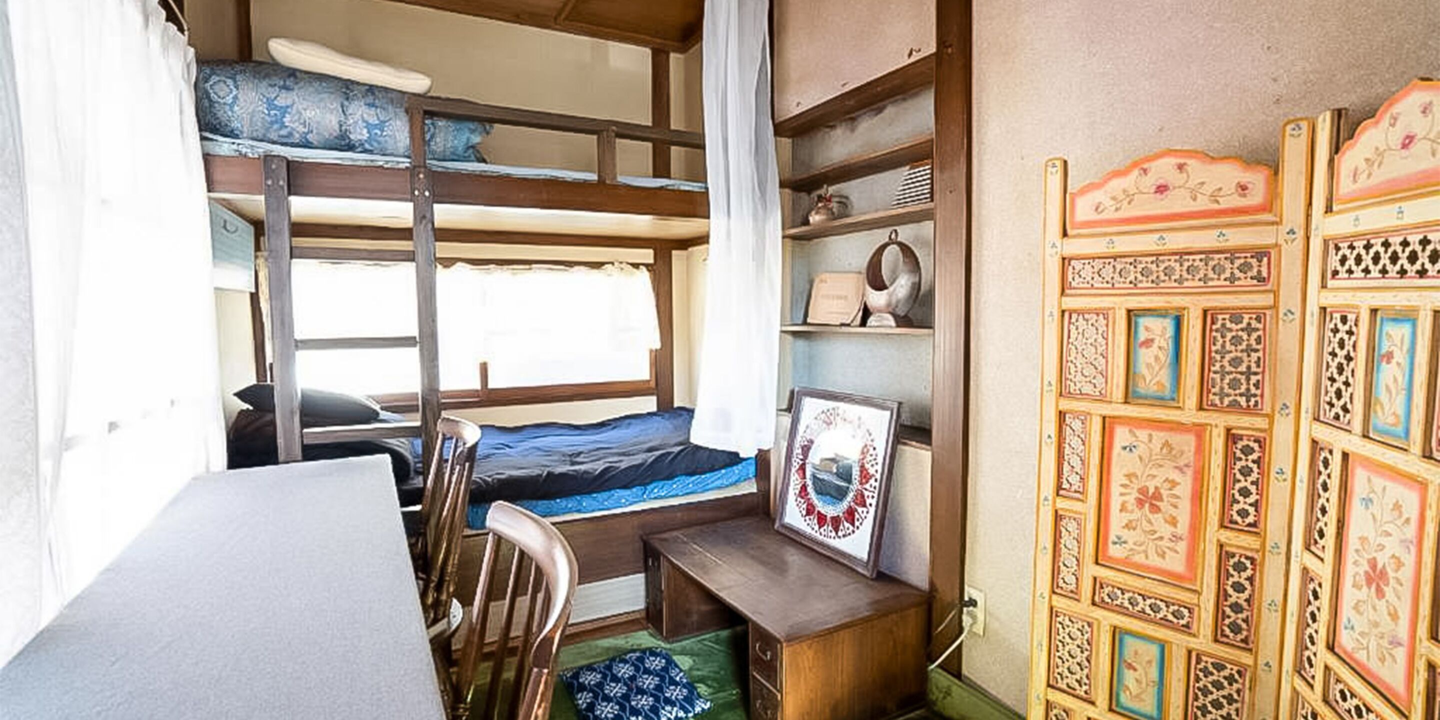 A bunk bed room with a desk and shelves, a framed picture, and a decorative wall panel.