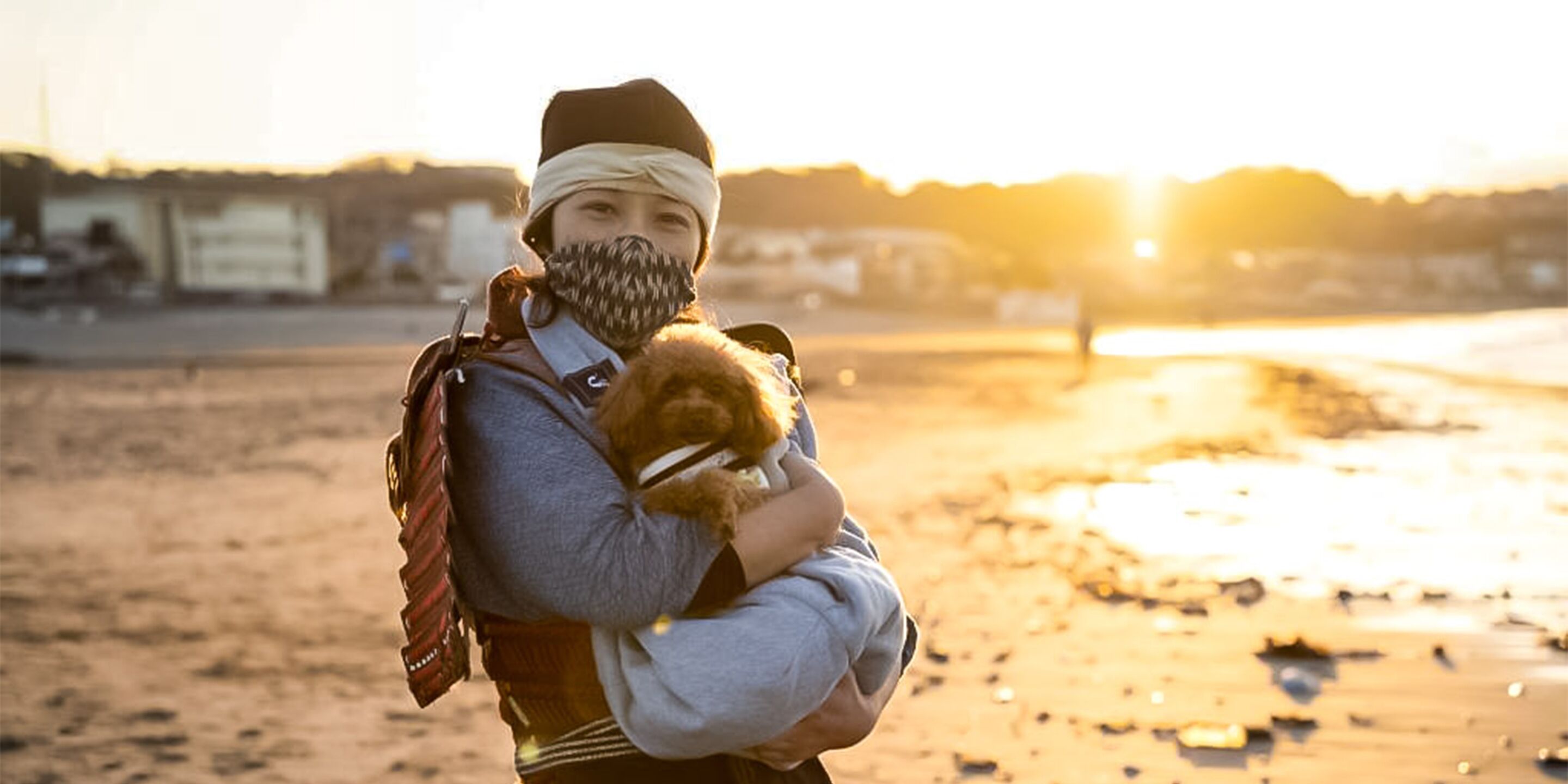 A person holding a small dog on a beach at sunset.
