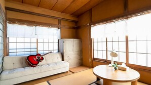 Una habitación tradicional japonesa con suelo de tatami, una mesa de madera baja, un sofá y una guitarra, además de puertas correderas.